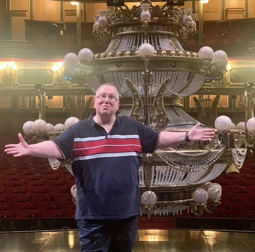 Peter Cavanna standing on stage at Phantom of the Opera, with the chandelier and seats behind him.