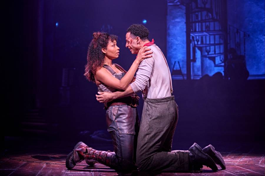 A man and woman are kneeling on the stage in an embrace. A spotlight lights them up.