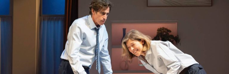 a man and a woman are stood behind a table. the woman on the left is laughing whilst the man on the left looks tense.