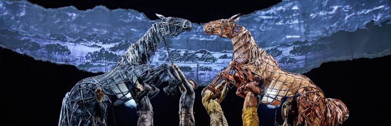 two horse puppets are rearing facing one another. They are held up by puppeteers.